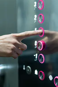 Ein magentafarbiger Knopf wird von einer Person im Aufzug gedrückt