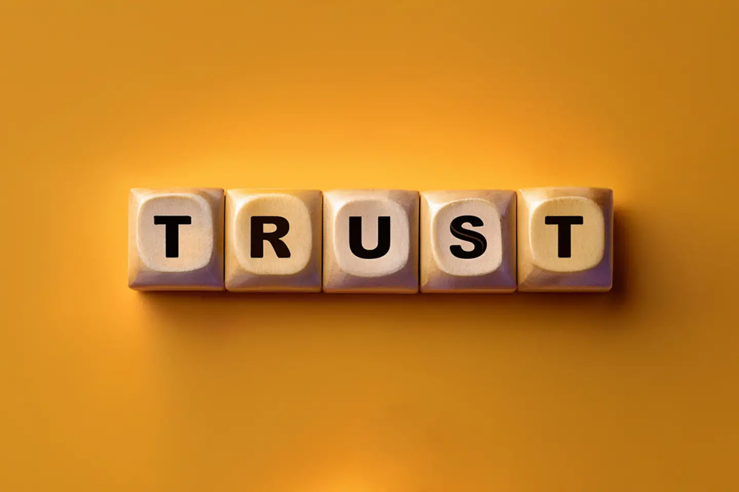 Fünf Würfel auf gelbem Grund mit den Buchstaben TRUST