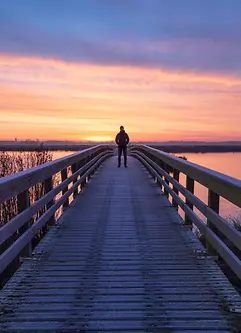 A man on a wooden bridge enjoying the view during a tranquil sunrise.