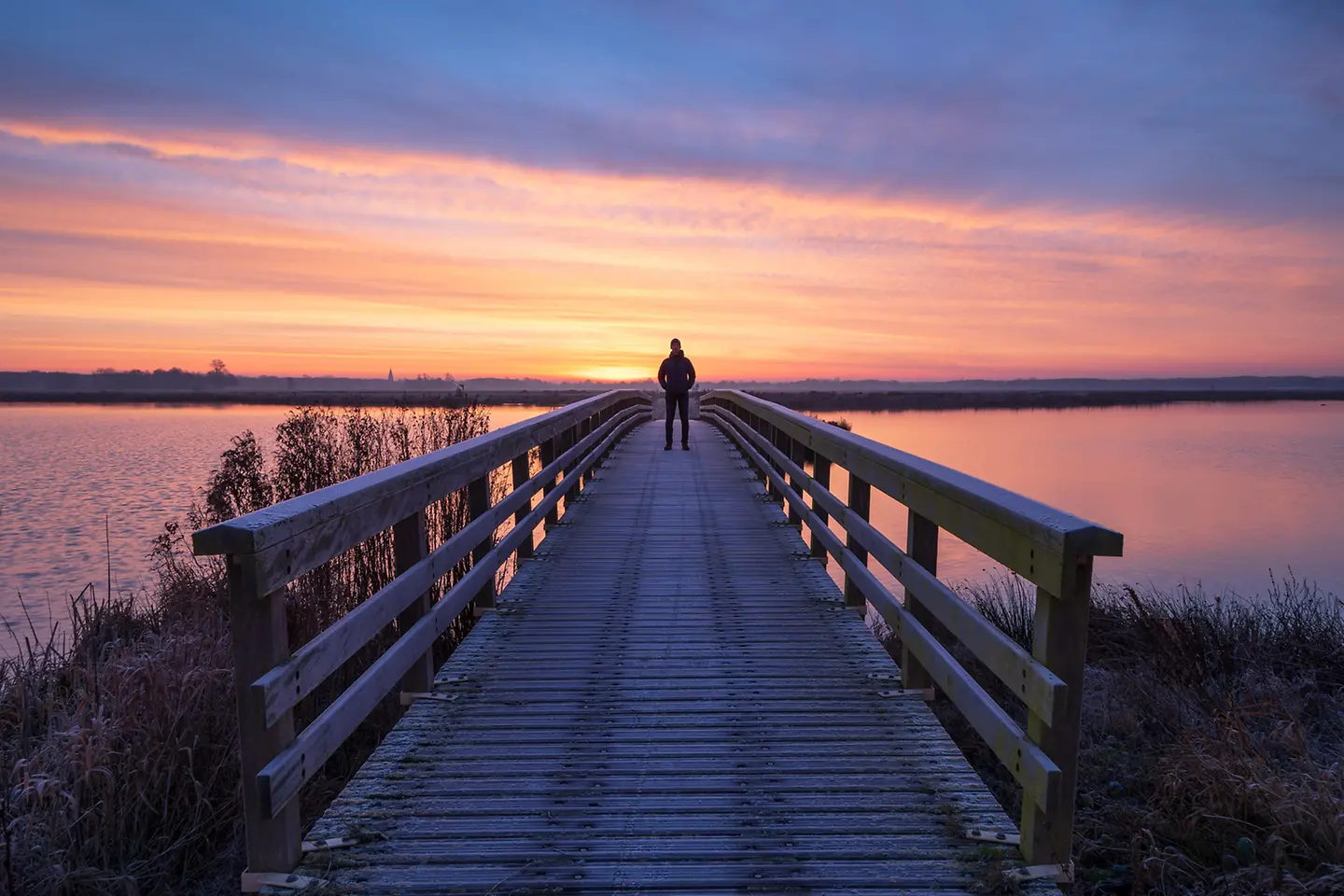 Ein Mann auf einer Holzbrücke, der die Aussicht bei einem ruhigen Sonnenaufgang genießt.