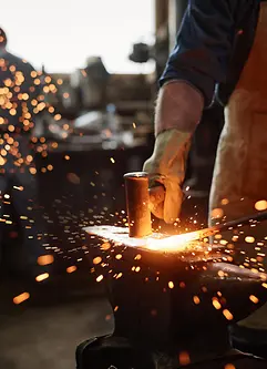 Close-up of blacksmith in apron working with hammer and iron in the workshop