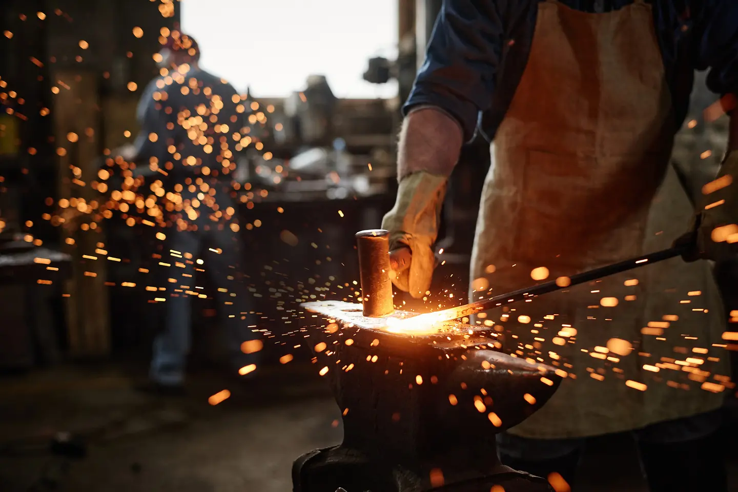 Primer plano de un herrero con delantal trabajando con martillo y hierro en su taller