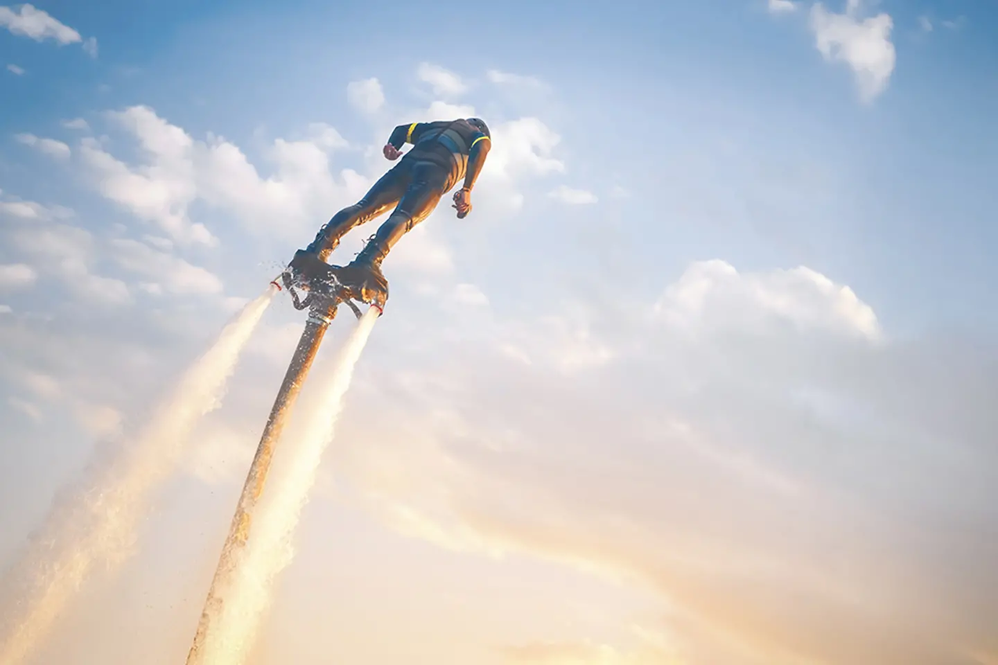 A flyboard athlete hovers over the water against the sunset sky, propelled by powerful jet streams of water.