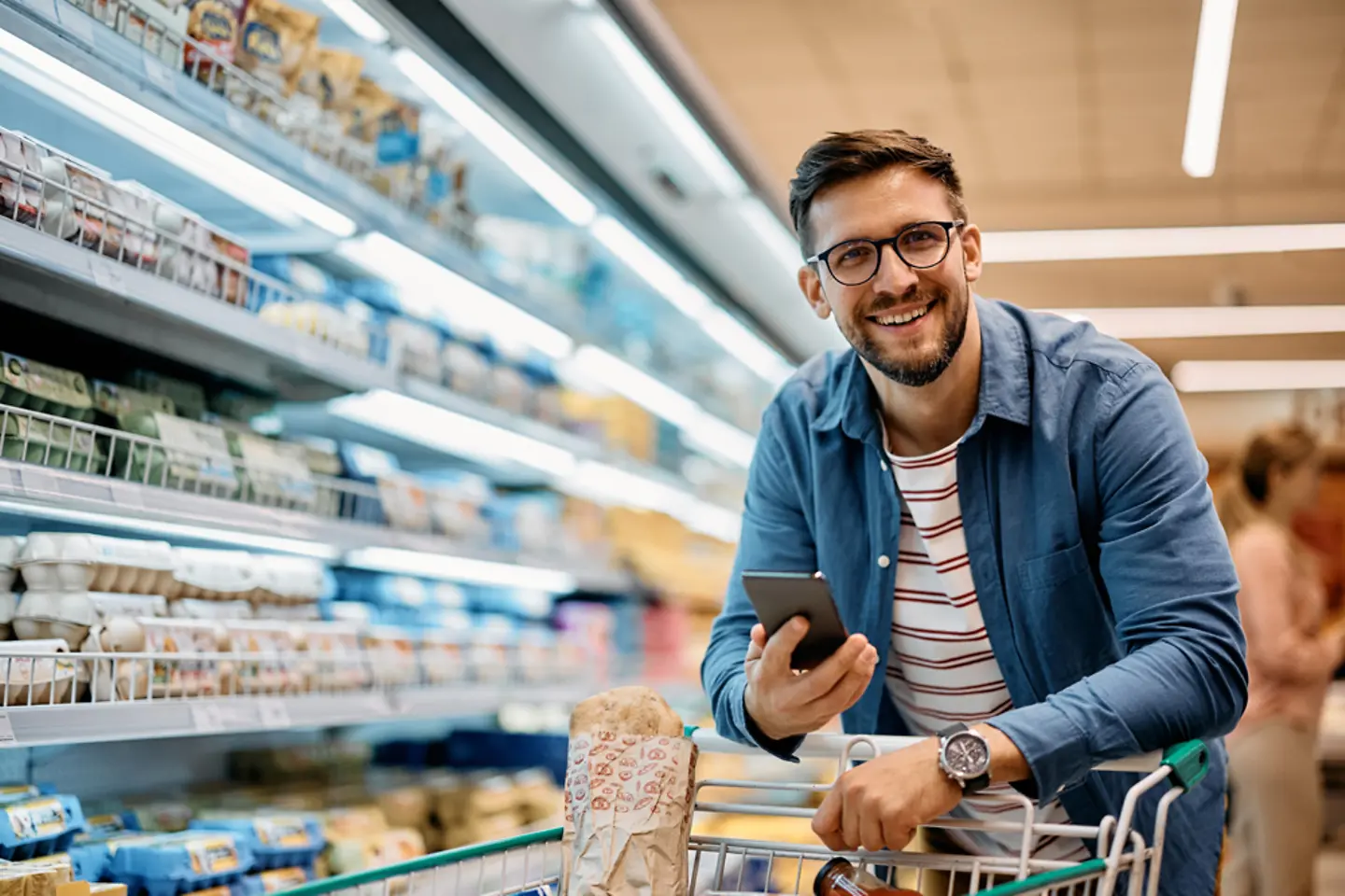 Hombre sonriente usando una aplicación móvil mientras hace la compra en el supermercado