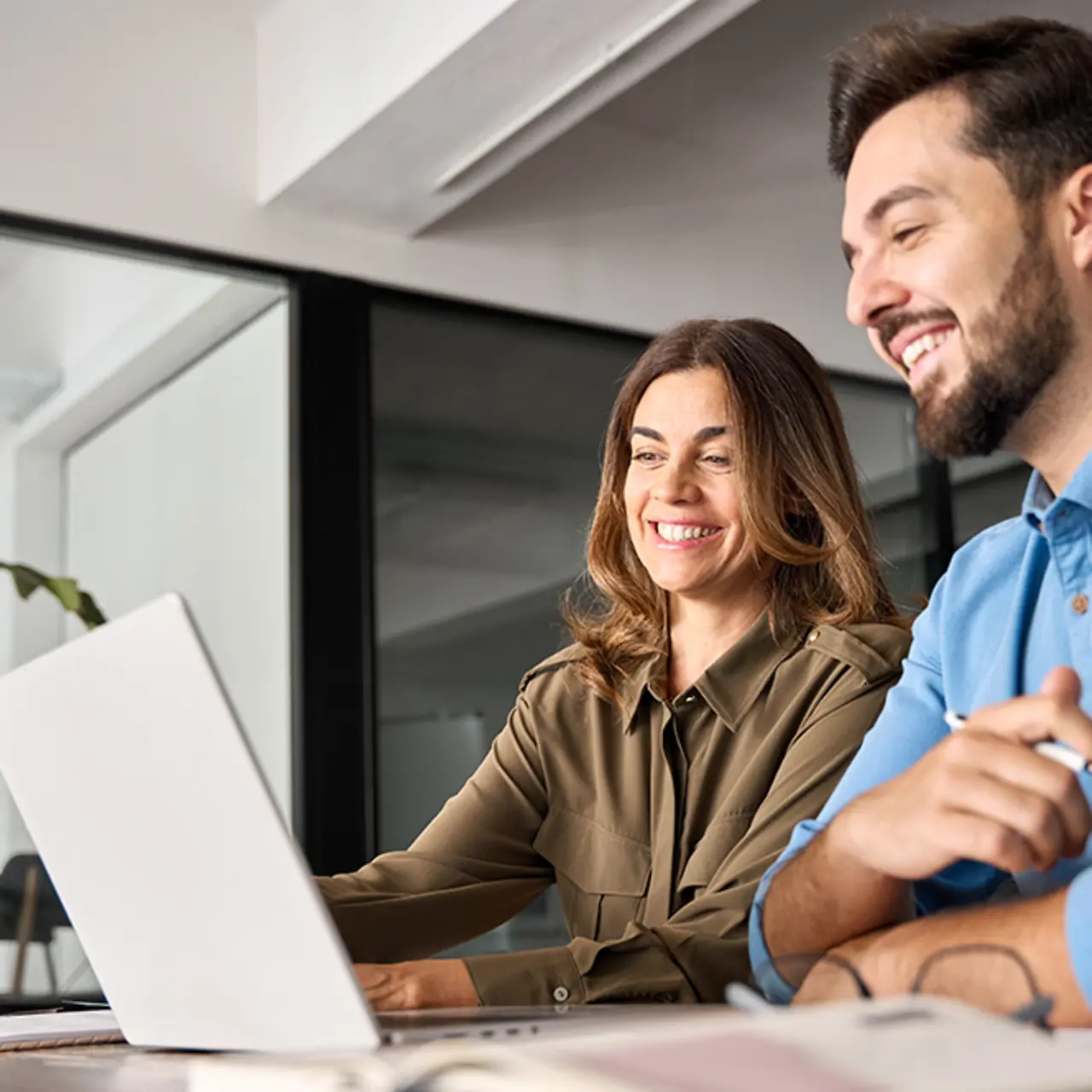 Dois profissionais sorridentes em uma conversa, trabalhando com laptops no escritório